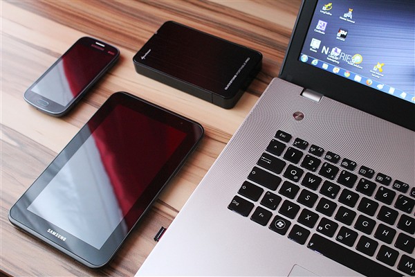 Ytterkanten av en PC, samt et nettbrett og mobiltelefon liggende ved siden av.